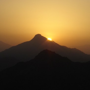The infant sun peeks out from behind a mountain peak