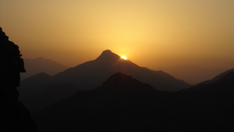 The infant sun peeks out from behind a mountain peak